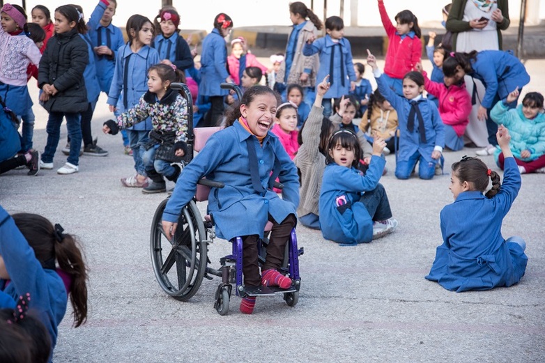  Spielende Kinder auf einem Schulhof. Im Vordergrund ein Mädchen, die einen Rollstuhl benutzt. Copyright: GIZ