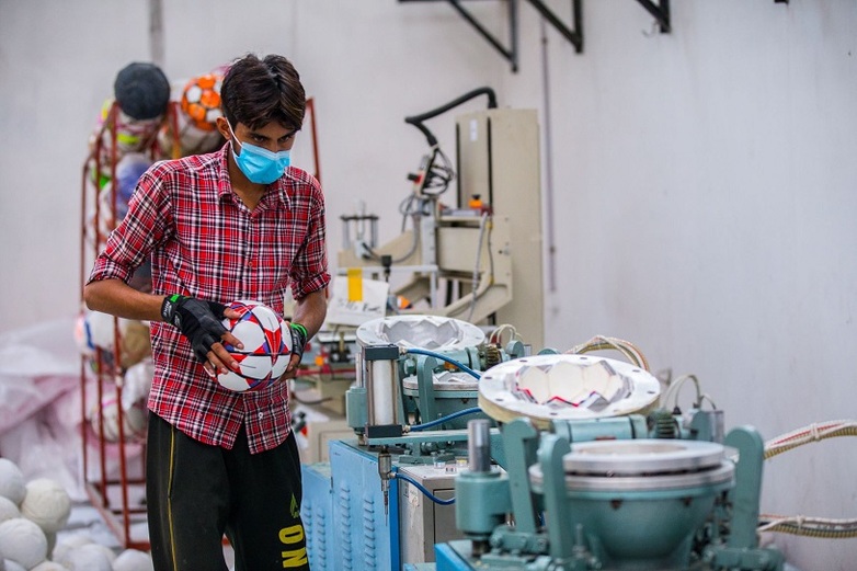 Ein junger Mann stellt in einer Fabrik einen Fußball her.