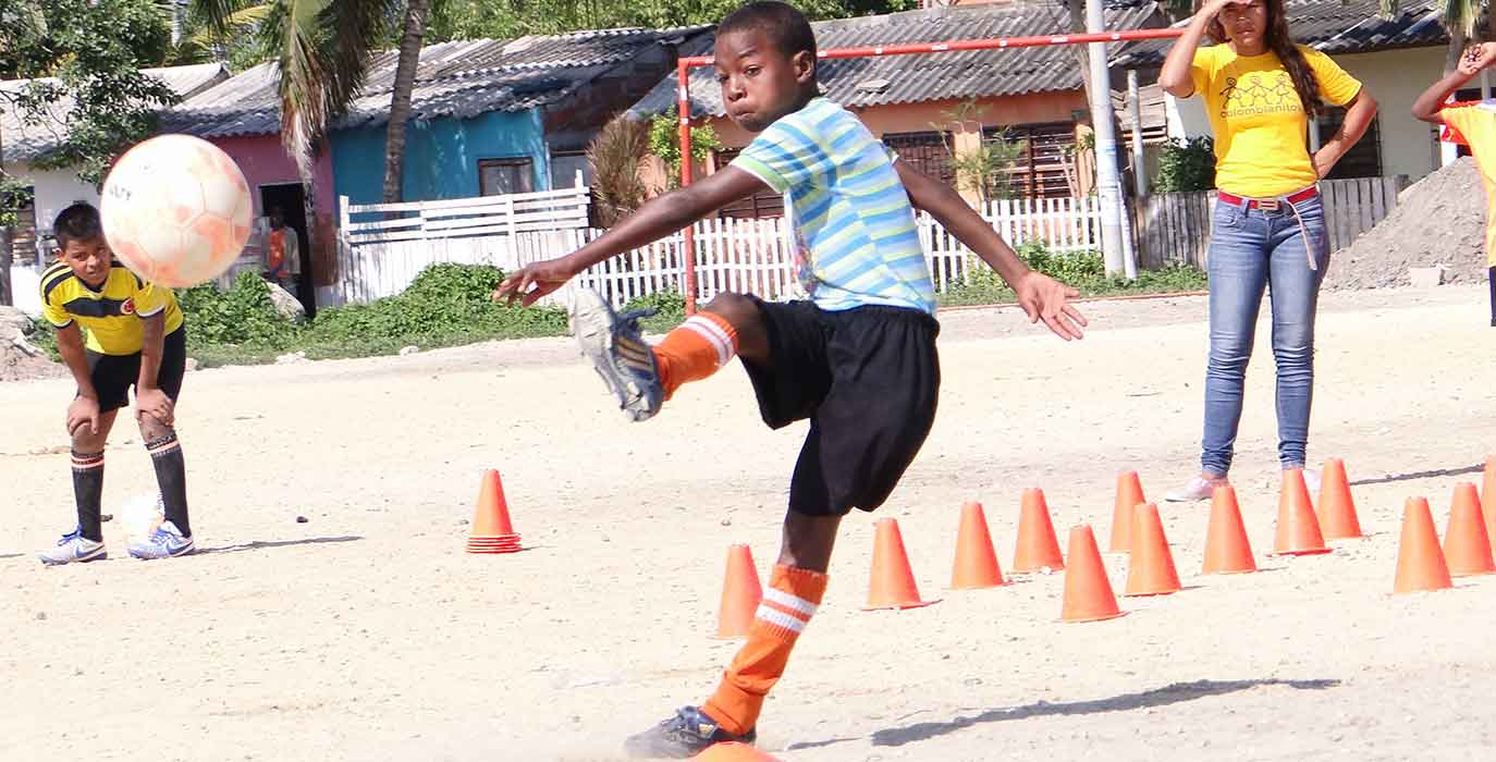 Kleiner Junge schießt Fußball auf einem Sandplatz
