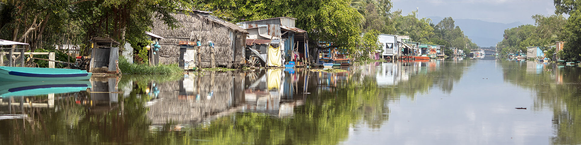 A river with huts, boats and trees lining its banks.