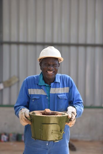 Un homme souriant en bleu de travail portant des équipement de sécurité tient dans ses mains un support de foyer. Droits d’auteur : GIZ