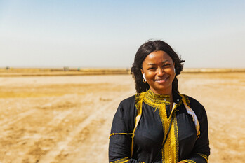 Une femme souriante avec des écouteurs dans un désert. Copyright : GIZ