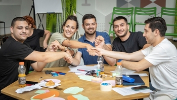 Five young people at a table holding hands.