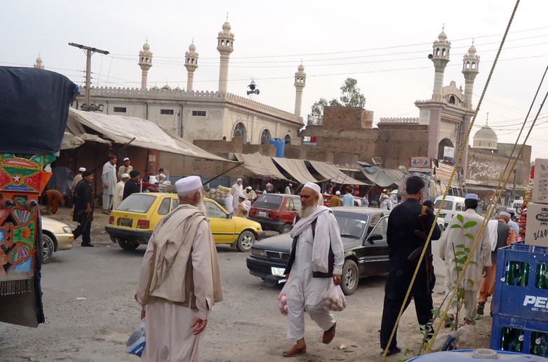 Men walking in a small town market in front of a mosque. 