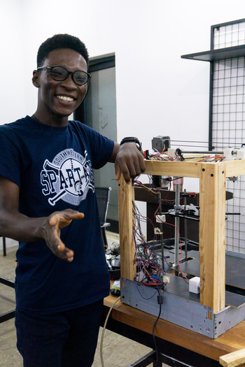 A young man beaming presents the shell of his 3D printer.
