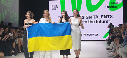 Four women are standing on a stage and holding a Ukrainian flag.