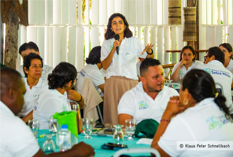 A woman speaks into a microphone at a seminar.