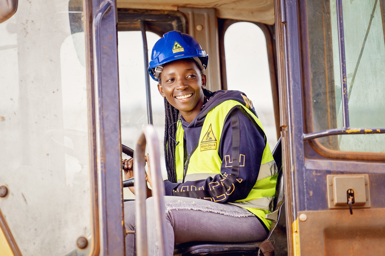 A person wearing a hard hat and vest sitting in a vehicle.