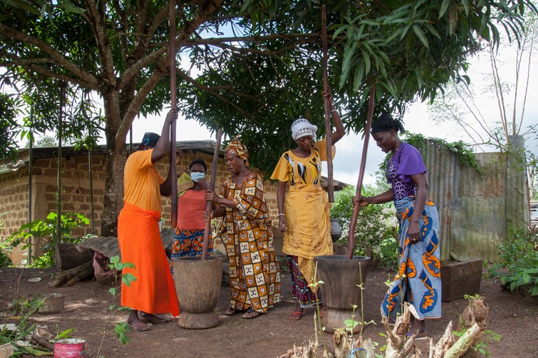 Frauen verarbeiten Makoré-Nüsse in großen Holzgefäßen zu Butter, die sie auf Märkten verkaufen.
