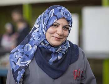 Une réfugiée syrienne en hijab et en uniforme de la GIZ sourit à la caméra. Elle suit une formation de plombière dans une école professionnelle jordanienne.