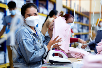 A worker holding up garments she has ironed. Copyright: Roman Koenig