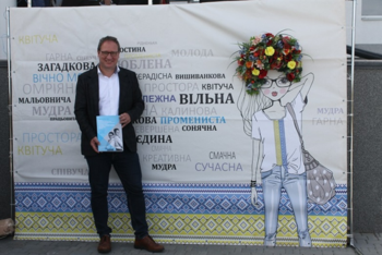 A man stands in front of a project wall and holds a brochure in his hand.