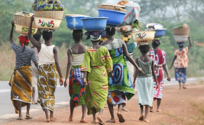 Women balance baskets on their heads as they stroll along a road