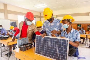 Four people in protective clothing hold a solar panel and learn about how it works. Copyright: GIZ