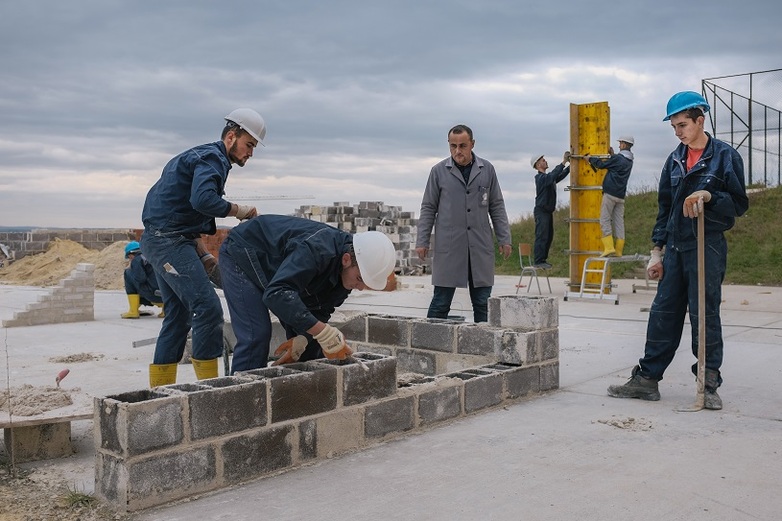 Pie de foto: Varios aprendices construyen un muro, mientras otros supervisan el trabajo, Centro de competencias de Skenderai, Kosovo