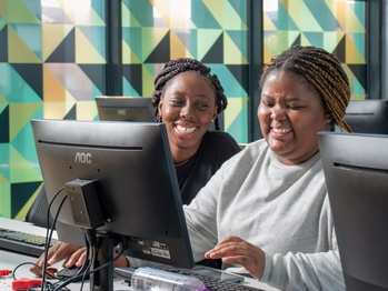 Two young women laugh while sitting at a computer