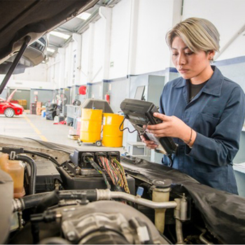 A trainee in the automotive industry standing in a garage and using a diagnostic scanner on a vehicle. 