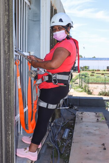 Une femme escalade une maison pour y installer des panneaux solaires.