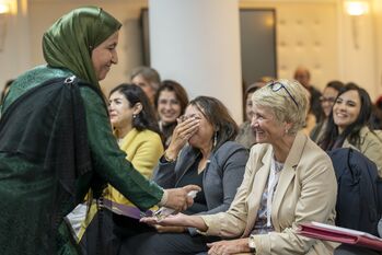 A woman sprays a sample of rose water on the arm of a woman in the audience.