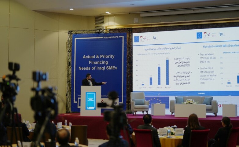 A GIZ staff member on a stage delivering a presentation on the financing needs of small and medium-sized enterprises in Iraq. Copyright: GIZ/Malte Mueller