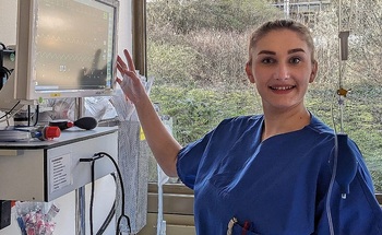 A person in blue scrubs standing in front of a computer.