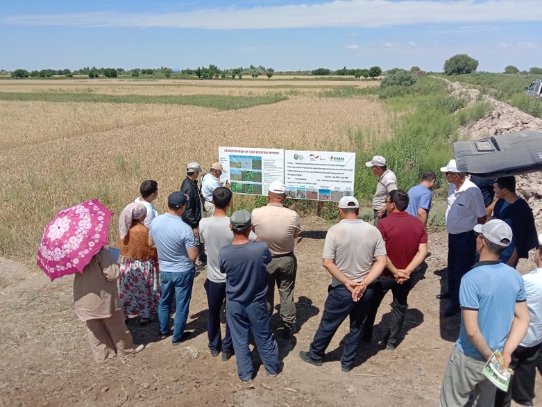 A group of farmers stands with a trainer in front of a panel in a field