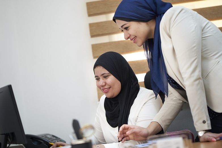Two women with hijab look at a screen smiling.
