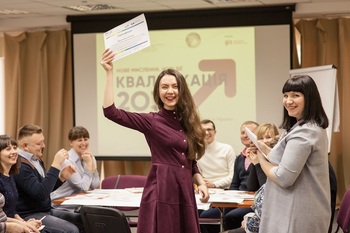 A woman standing in front of a presentation smiles while holding up a document. Other people beside and behind her smile into the camera. Copyright: GIZ