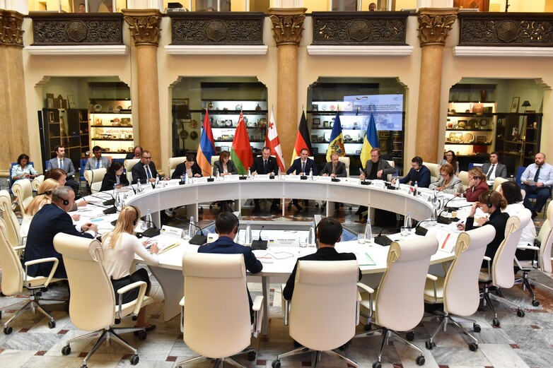 People at a conference table with flags in the back.