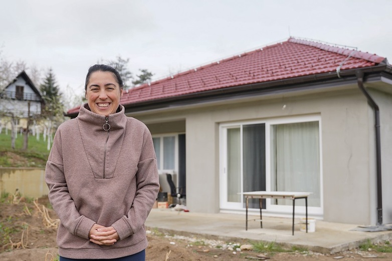A smiling woman stands in front of her house in Bosnia and Herzegovina after energy efficiency measures have been carried out on the building. 