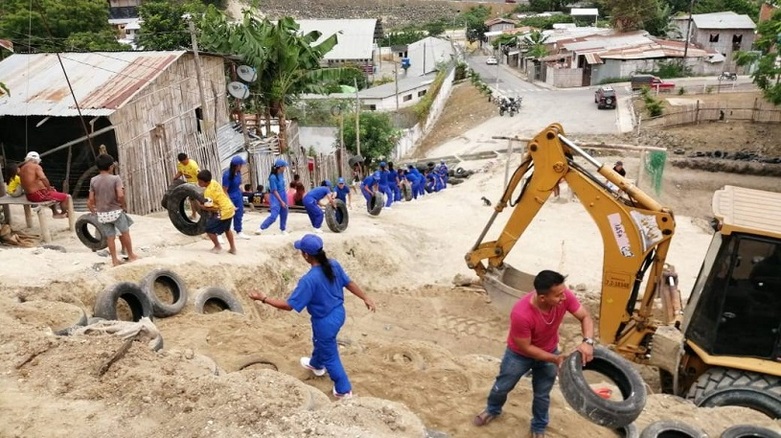 A building site with an excavator. People transport car tyres in a chain. 