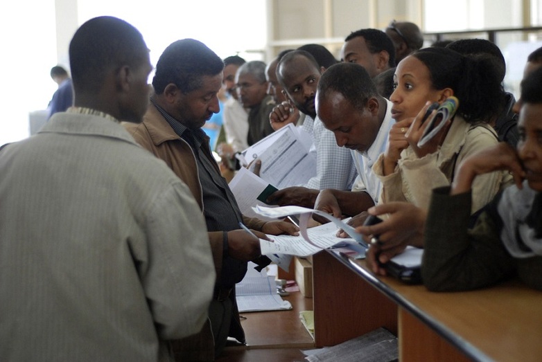 Many people with documents in their hands stand in front of a counter, behind which two men accept the documents. Copyright: GIZ, Michael Tsegaye, Good Governance