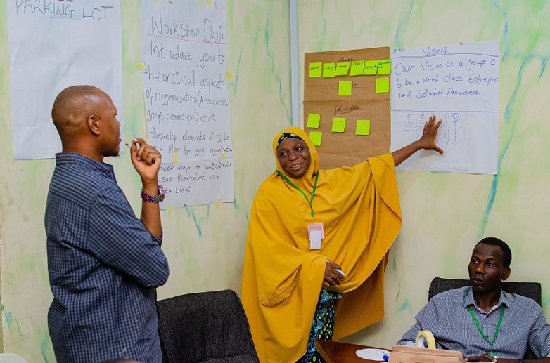 At a training course for corporate service providers, a woman points to a poster while a man listens to her and looks at the poster.