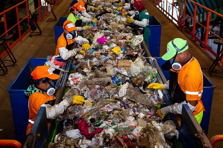People in protective clothing sort trash on an assembly line.