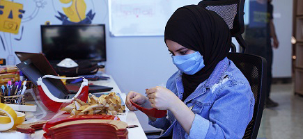A woman in a headscarf and face mask sews face masks.