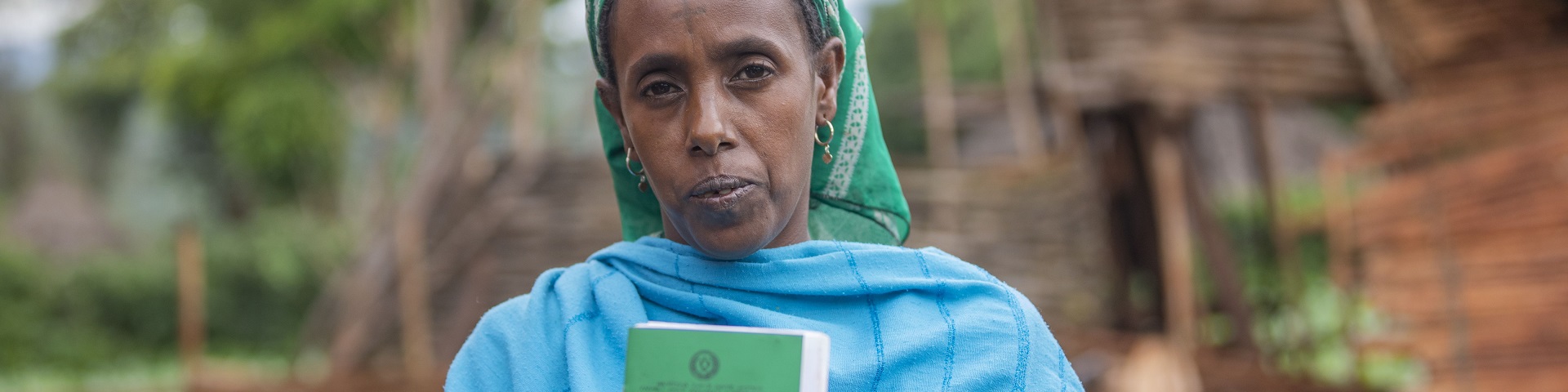 Front view of an Ethiopian woman holding her land certificate up for the camera.
