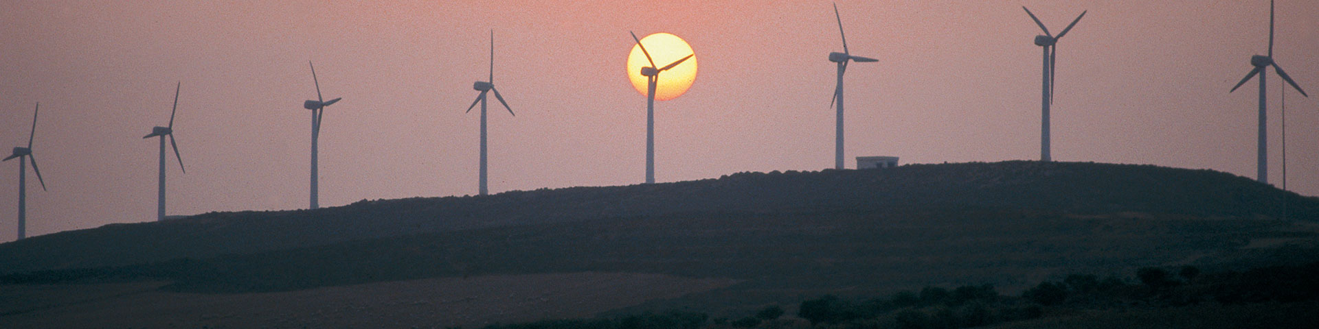 A row of wind turbines stands on a hill at dusk.