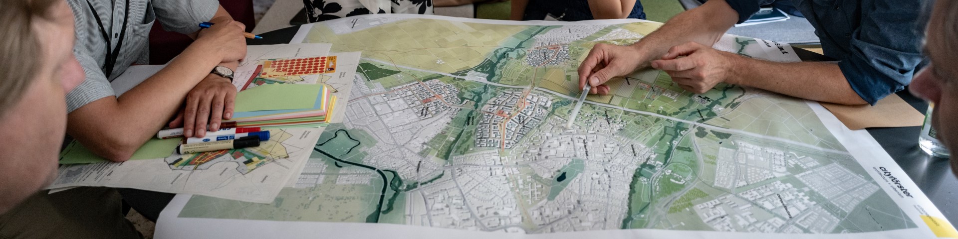 Several people sit around a city map and mark places on it.