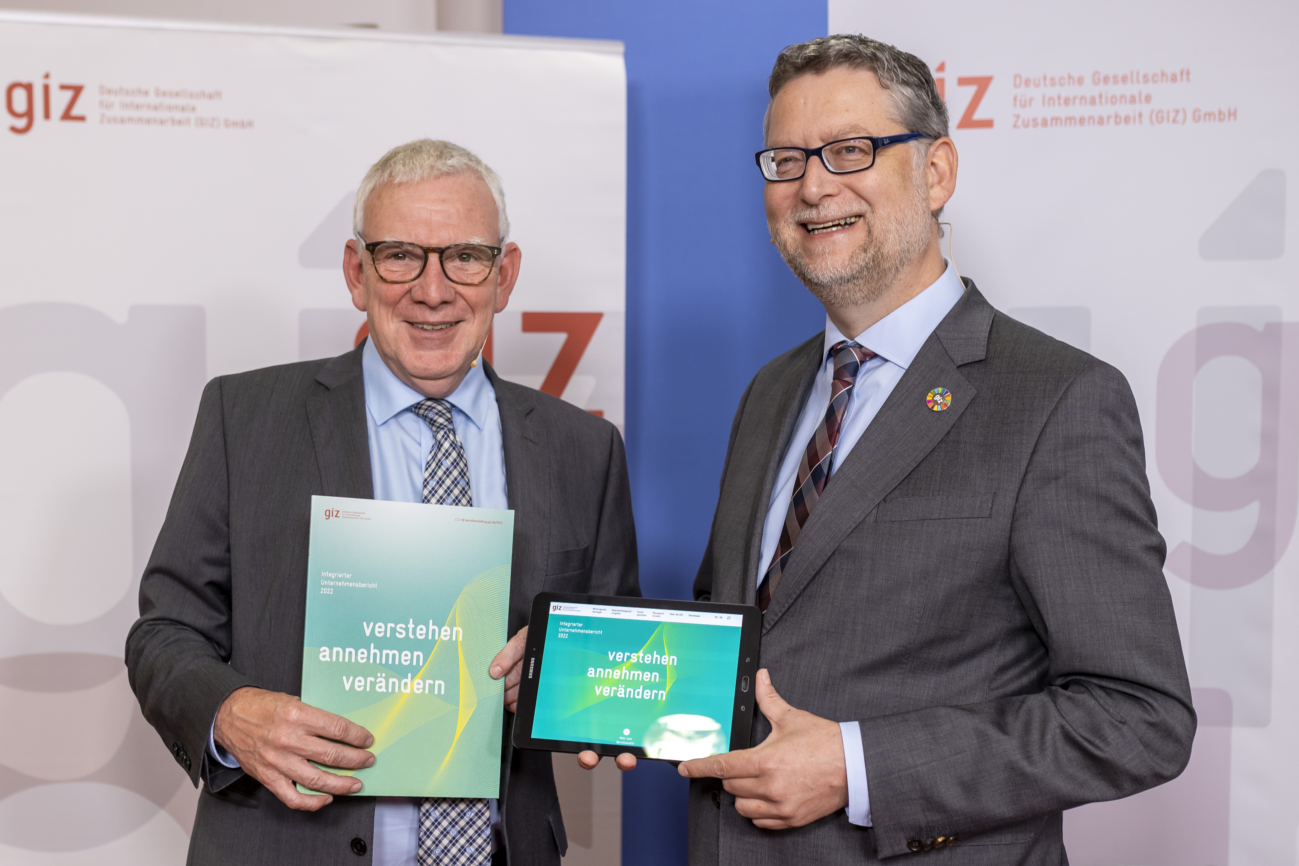 Jochen Flasbarth and Thorsten Schäfer-Gümbel in front of GIZ banners holding the GIZ Integrated Corporate Report 2022 in their hands.