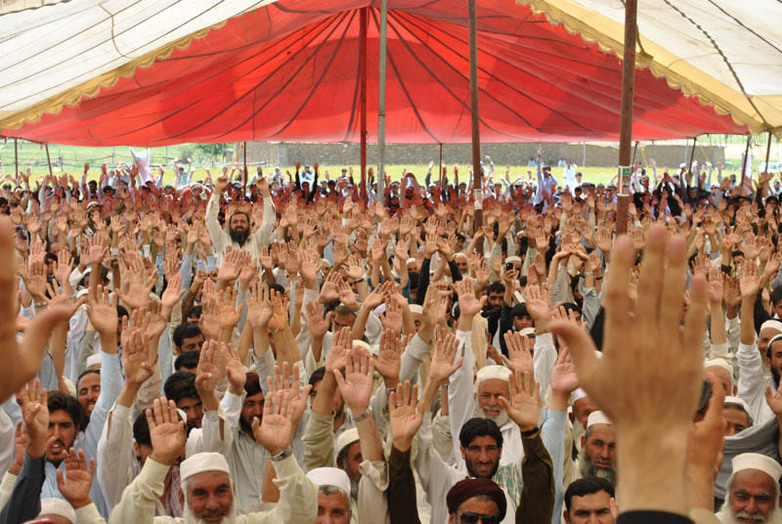 Men in traditional clothing cast a vote by rising their hands. 