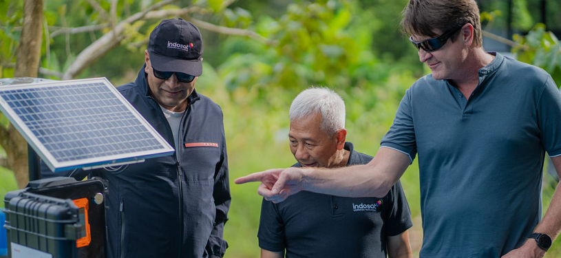 Three men inspect a solar panel in the forest.