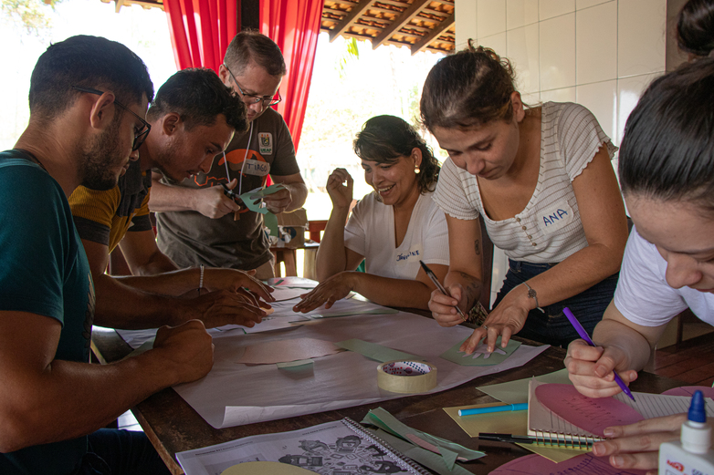 Several people stand at a desk and use markers on a map.