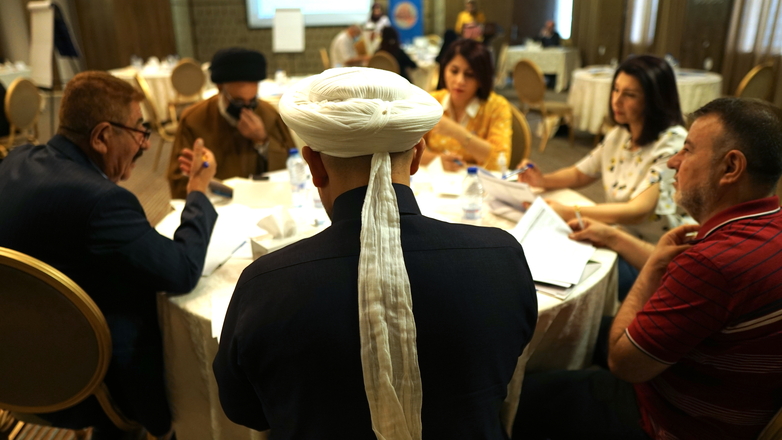 Women and men of different religions sit at a round table talking to one another. Copyright: GIZ