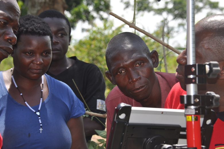 Five people look at the screen of a device surveying land in central Uganda.