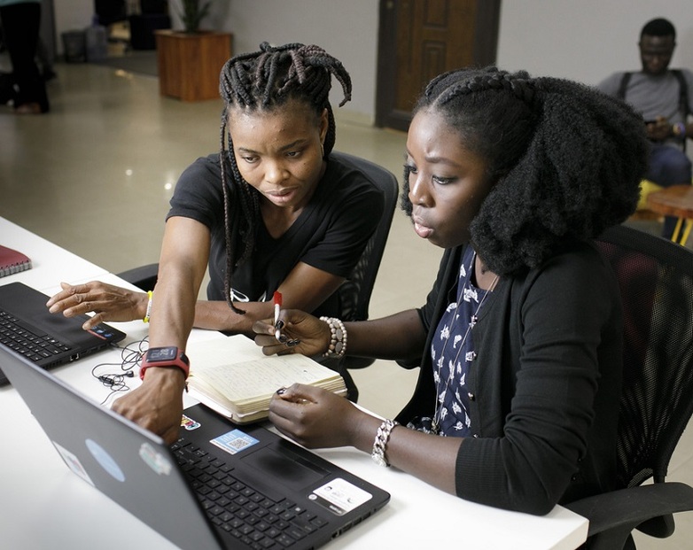 Dos mujeres trabajan con computadoras portátiles y conversan sobre una tarea, centro de creación conjunta en Lagos, Nigeria