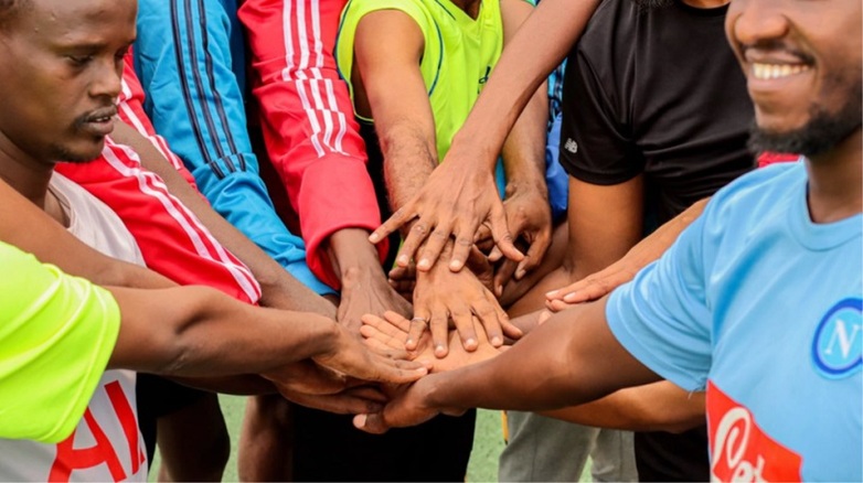Football coaches take part in a team-building exercise and place their hands on each other. Copyright: GIZ / Andrew Oloo