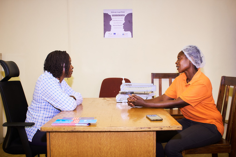 Two women sitting across from each other at desk: protagonist Rita Mulenga receives free legal advice.