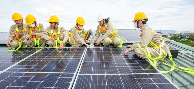 Young people in working gear are installing solar panels on a roof.