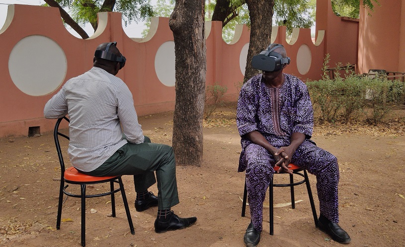 Two men sitting on stools wearing virtual reality goggles.