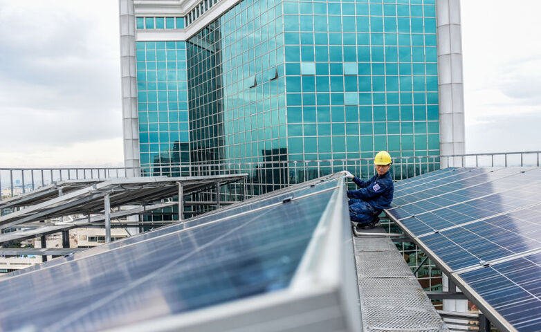 Eine Person in Arbeitskleidung und mit Sicherheitshelm installiert Solarmodule auf einem Dach in Vietnam.